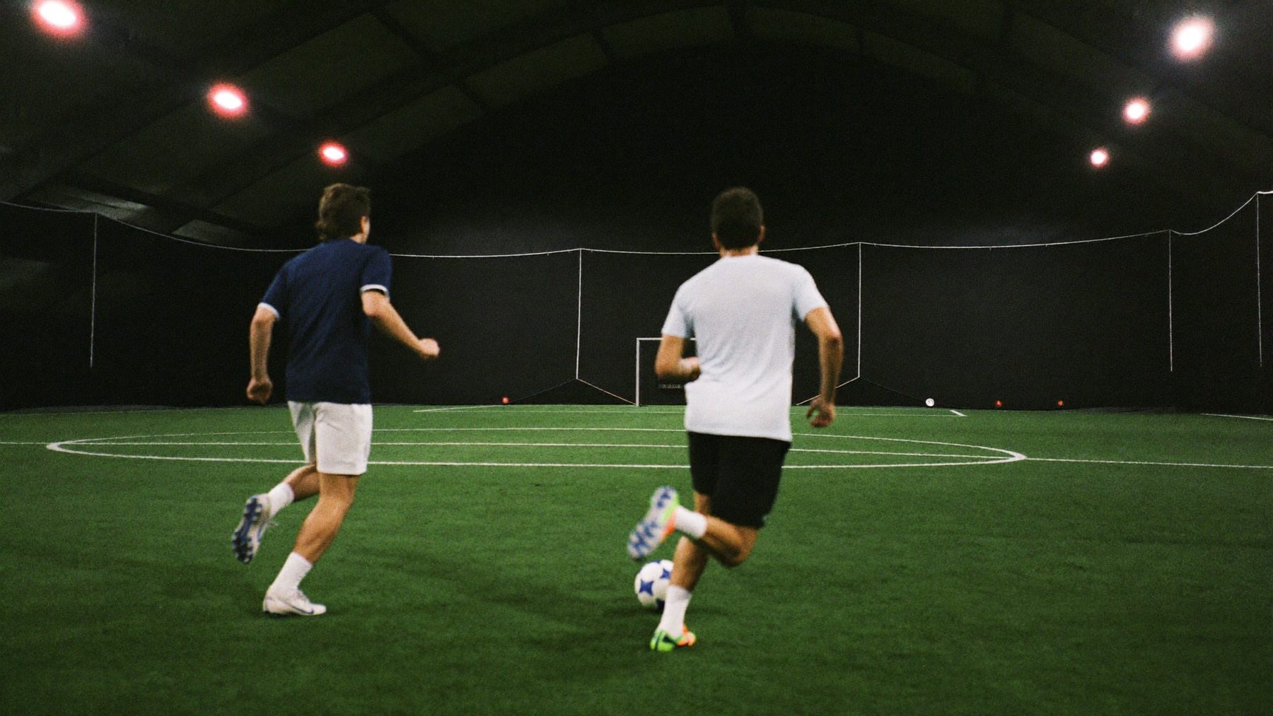 Two players chasing the ball on an indoor field at night