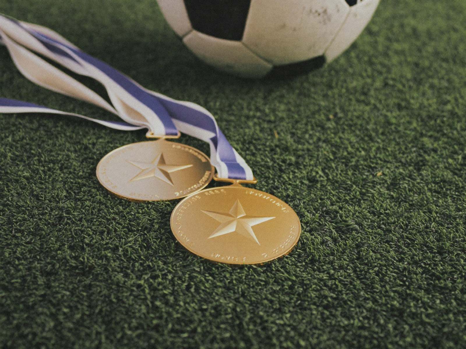 Gold medals and a soccer ball on the turf