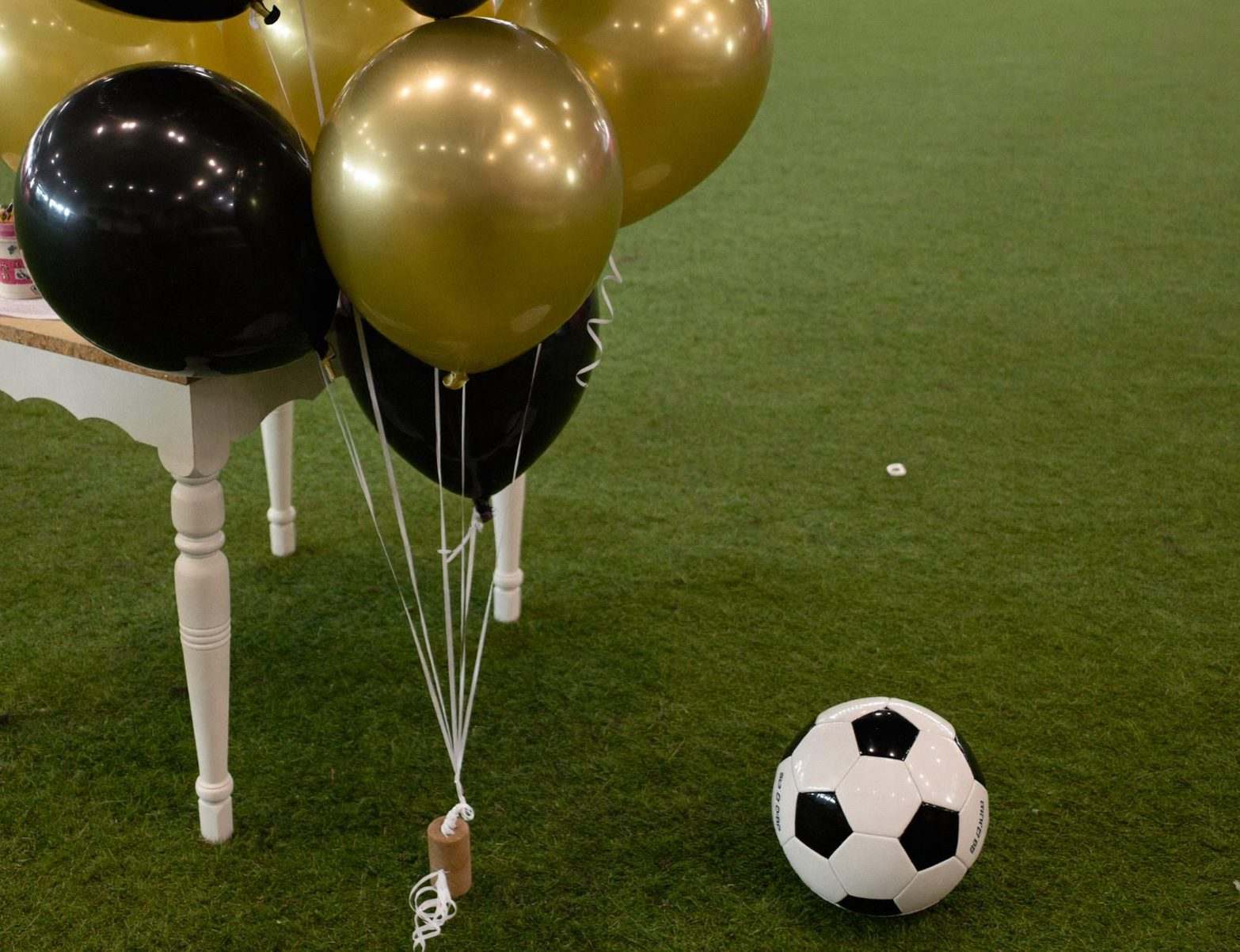 Black and gold balloons and a soccer ball on turf
